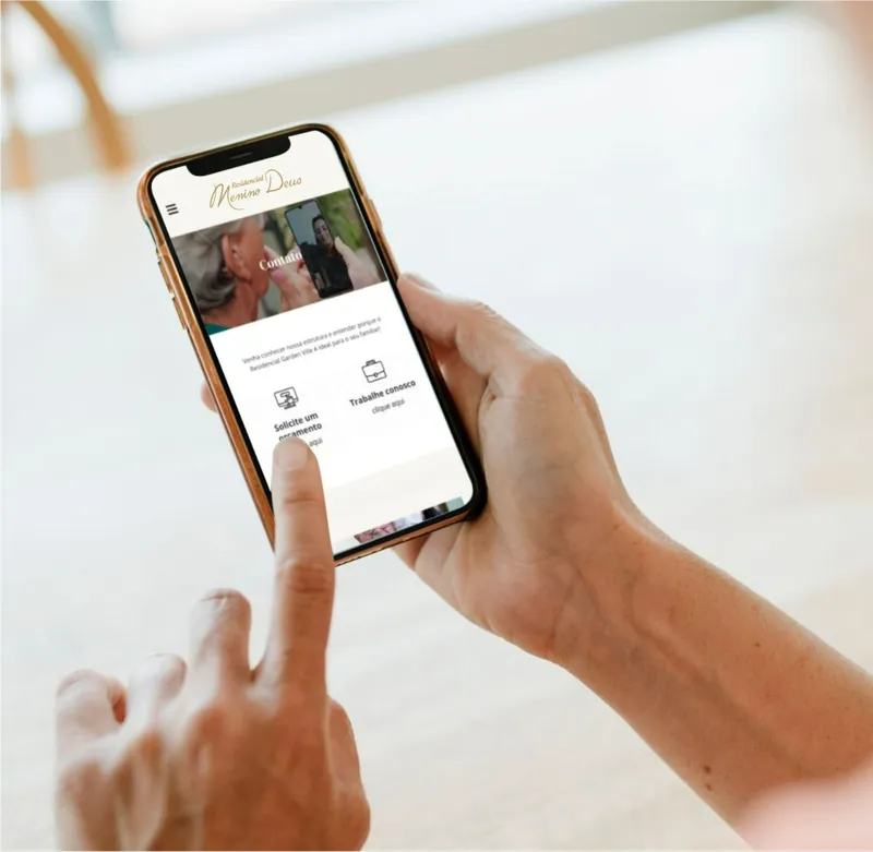 Mão segurando um celular com o site do Residencial Menino Deus aberto na página de contato