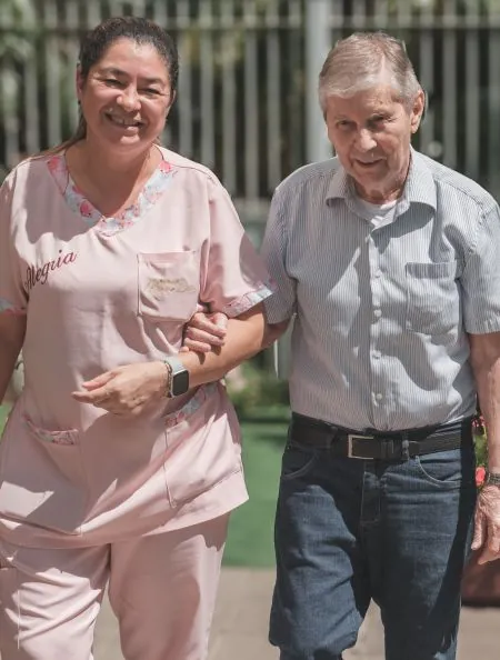 Cuidadora do Residencial Menino Deus caminha de braço dado com um idoso na área externa, em Porto Alegre